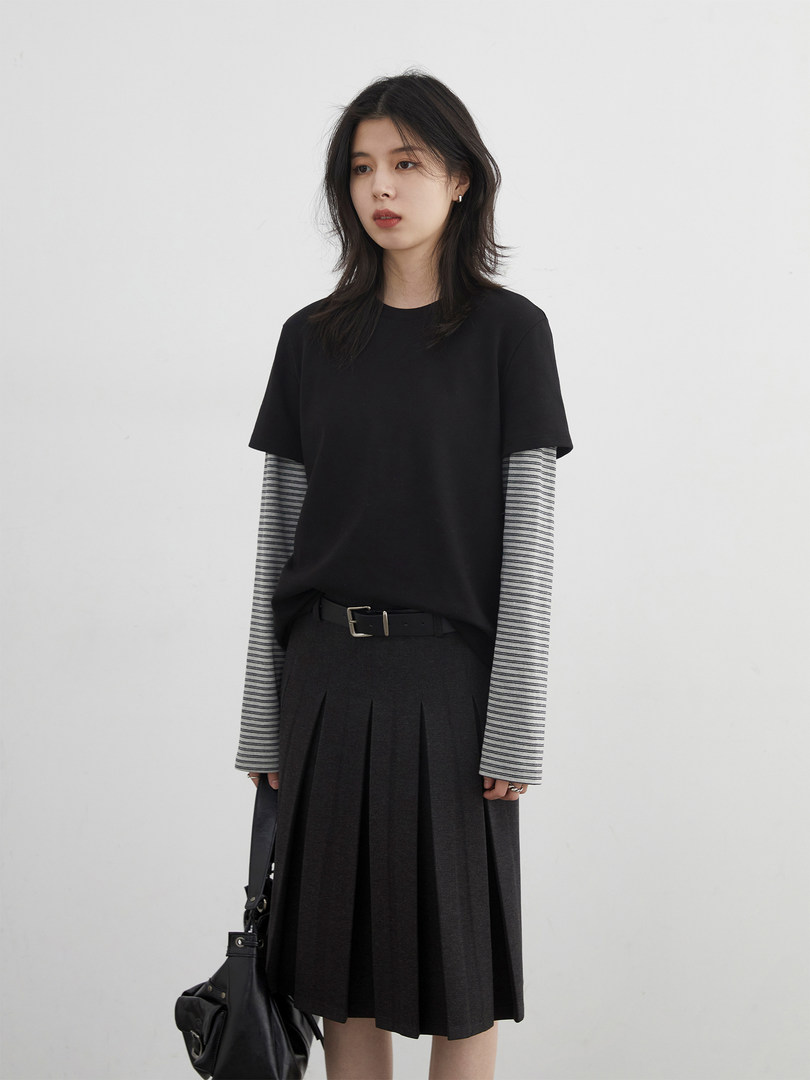 Model wearing a black layered long-sleeve top and pleated skirt outfit