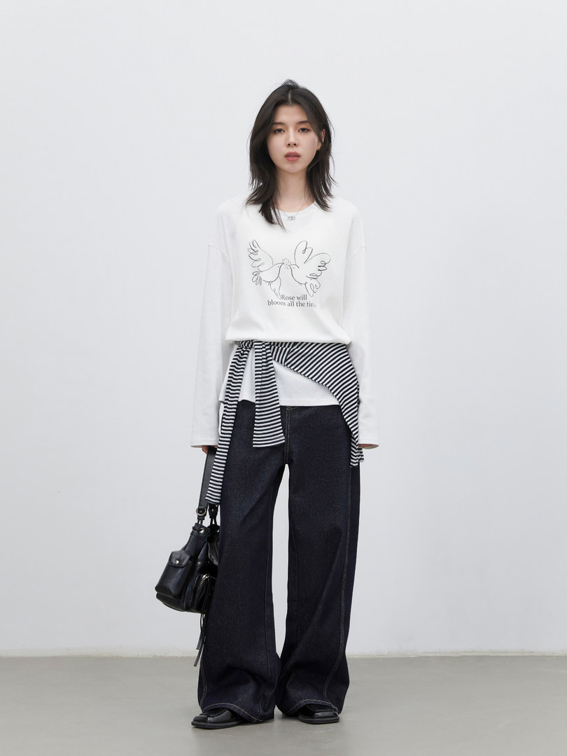 Model wearing a white graphic long-sleeve top with layered striped detail and dark wide-leg jeans