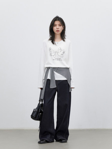 Model wearing a white graphic long-sleeve top with layered striped detail and dark wide-leg jeans