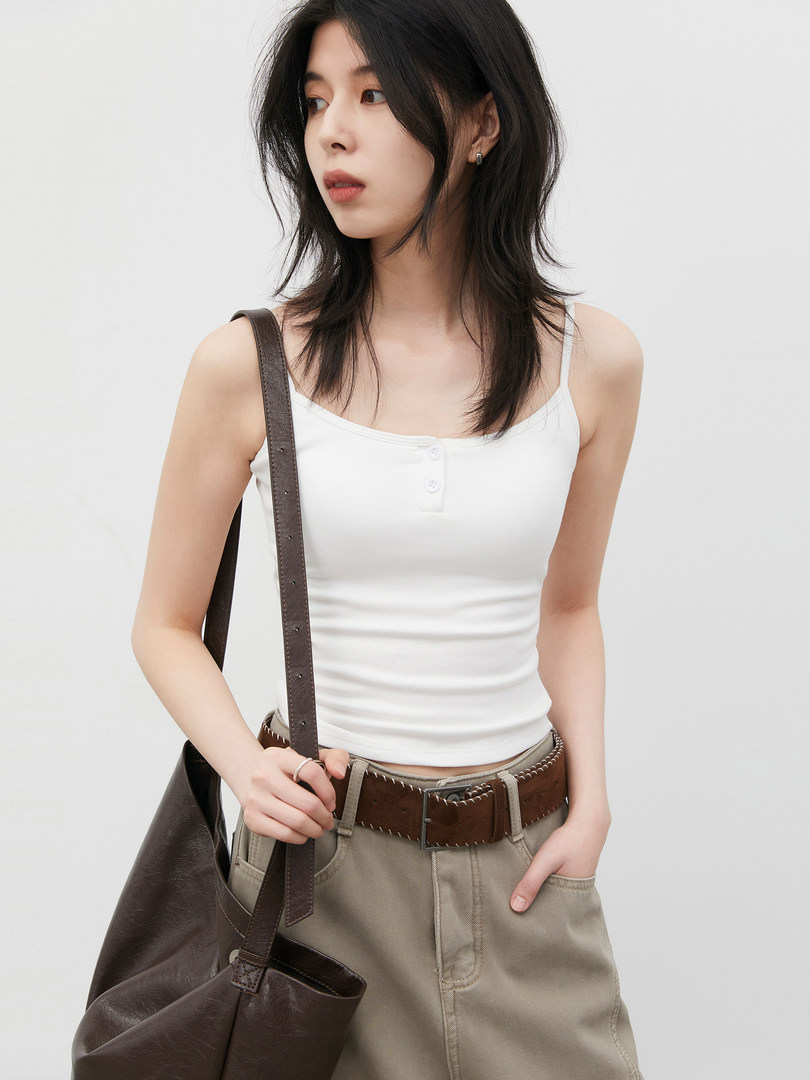 Model wearing a white sleeveless tank top with khaki pants and a dark brown shoulder bag