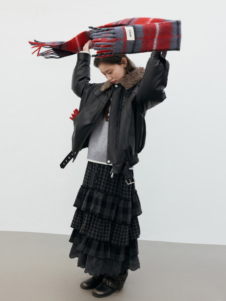 Model wearing a black leather jacket, layered plaid skirt, boots, and a red plaid scarf