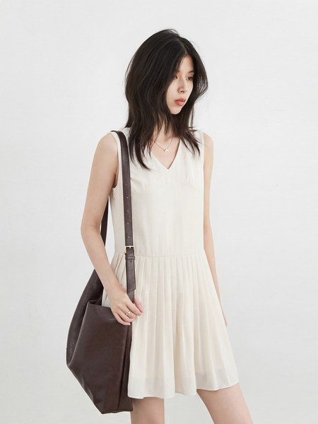 Woman wearing a cream sleeveless pleated dress with a brown shoulder bag
