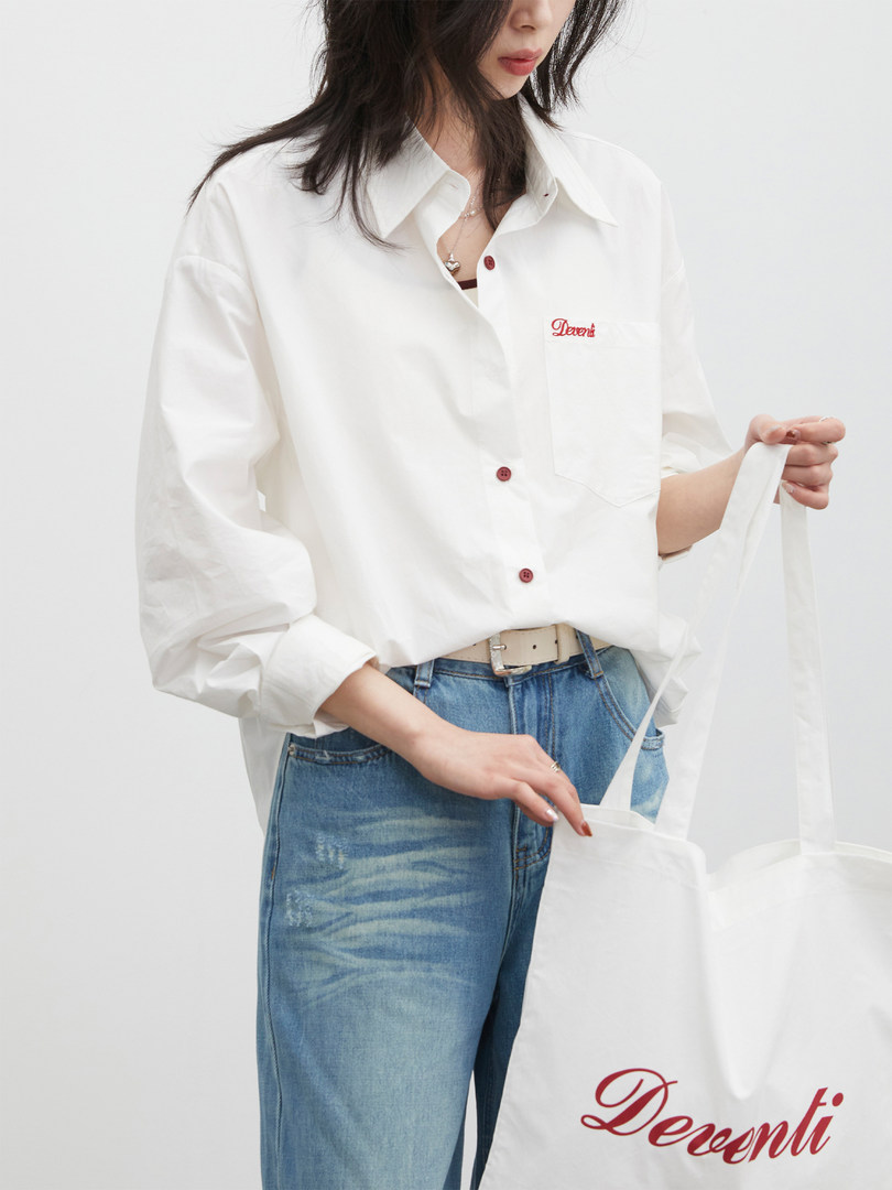 Model wearing a white button-up shirt with blue jeans and a tote bag