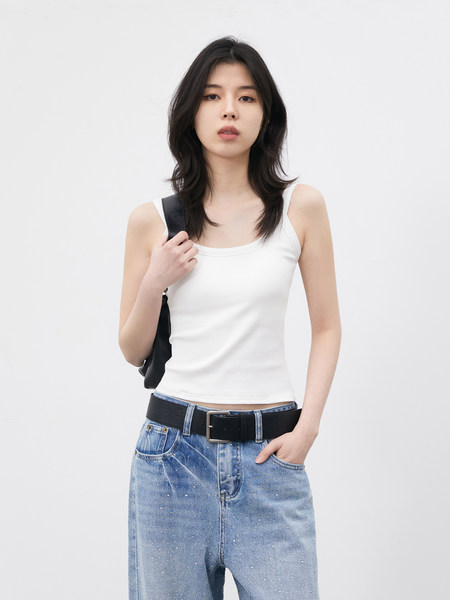 Model wearing a white tank top with blue jeans and a black bag strap