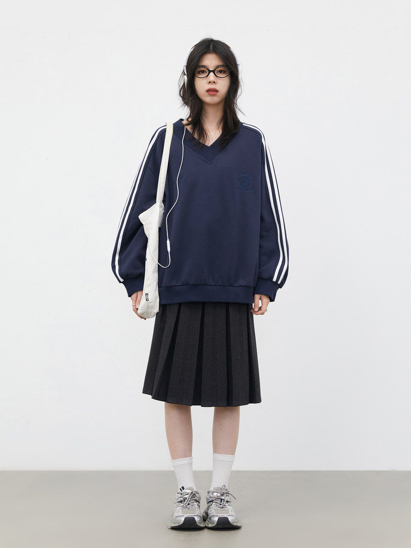 Model wearing a navy oversized sweatshirt with white stripes, a black pleated skirt, and sneakers