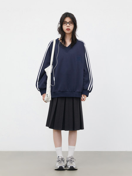 Model wearing a navy oversized sweatshirt with white stripes, a black pleated skirt, and sneakers