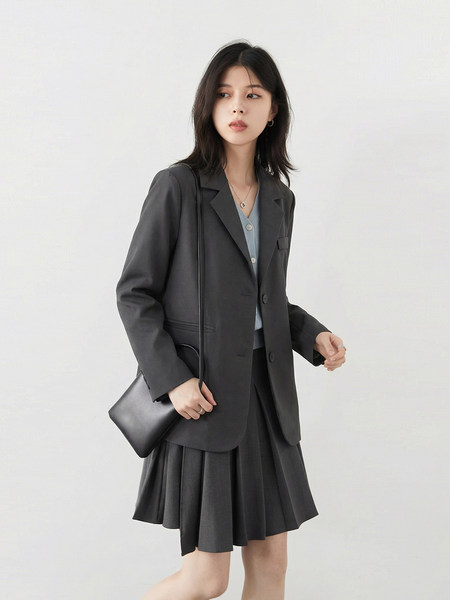 Model wearing a dark blazer with a pleated skirt and shoulder bag