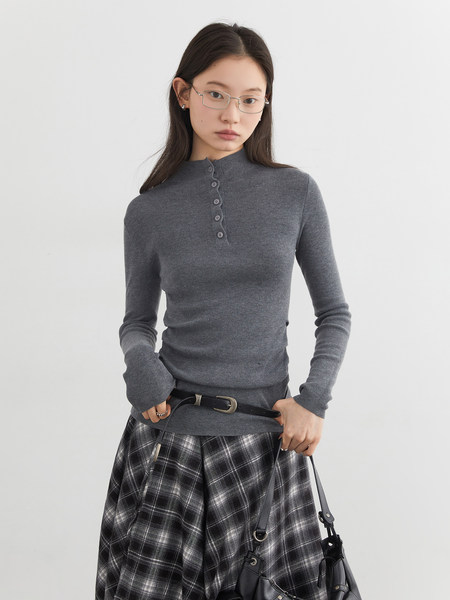 Model wearing a gray long-sleeve button-front knit top with a plaid skirt and black bag