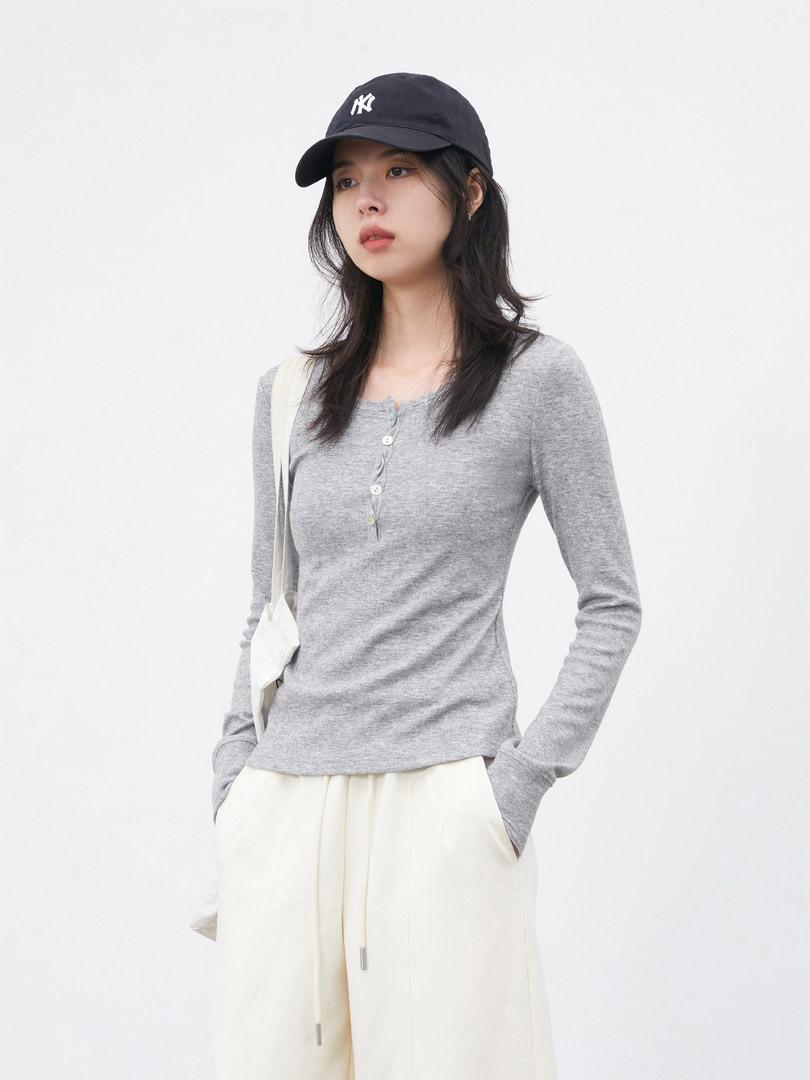 Model wearing a gray long-sleeve henley top with cream pants and a black cap