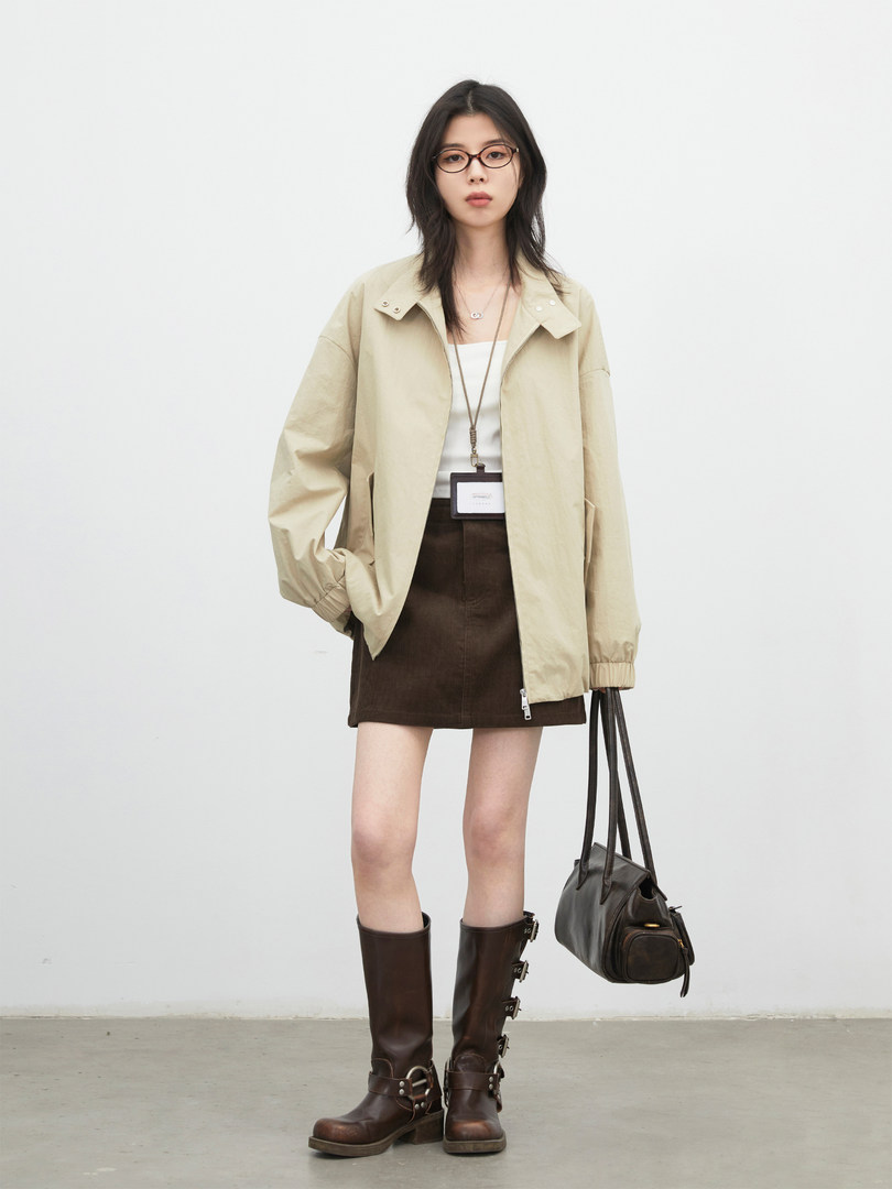 Model wearing a beige jacket with a brown skirt, tall leather boots, and a black shoulder bag