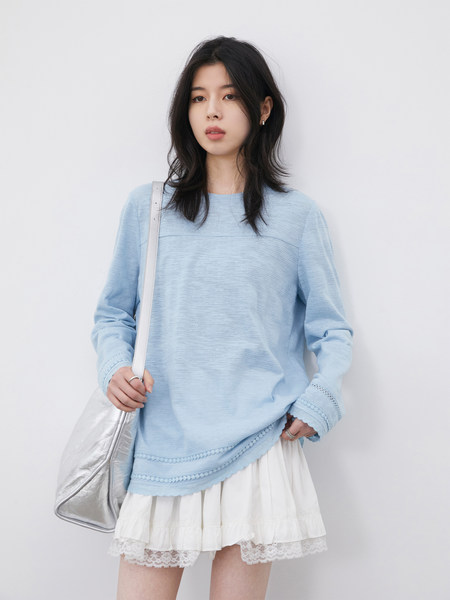Model wearing a light blue long-sleeve top with a white lace-trim skirt and silver shoulder bag