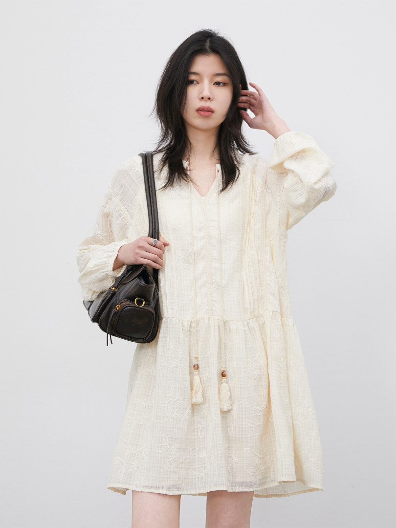 Model wearing a cream long-sleeve dress with a black shoulder bag