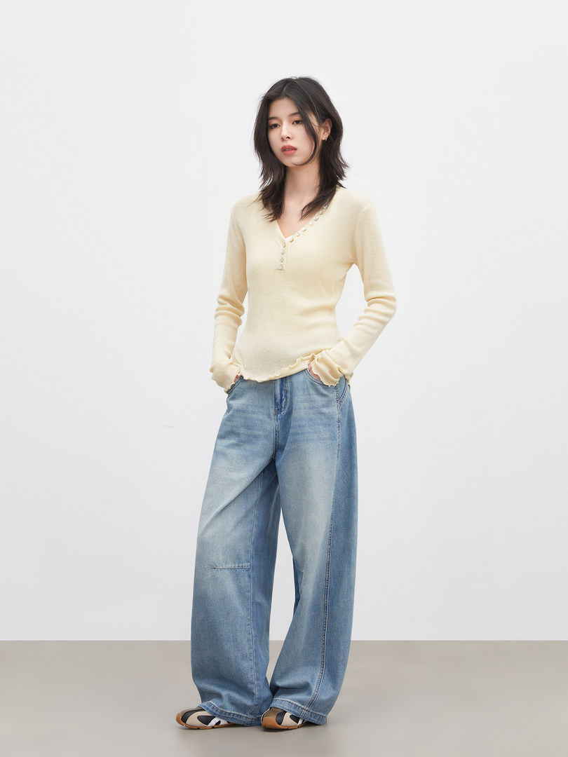 Model wearing a cream long-sleeve V-neck top with wide-leg blue jeans