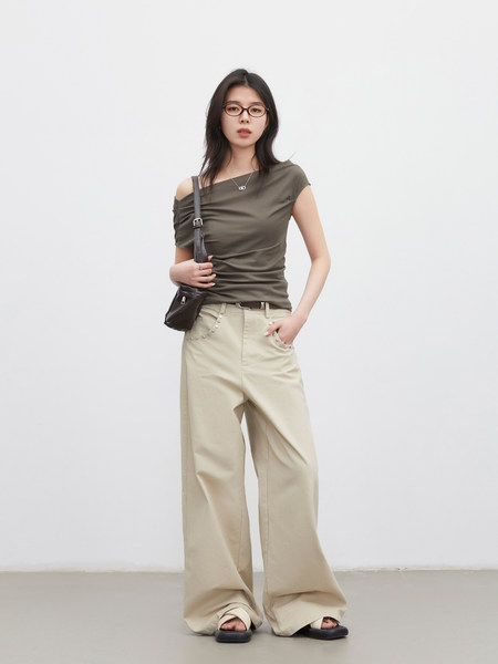 Model wearing an olive one-shoulder top with beige wide-leg pants and a black shoulder bag
