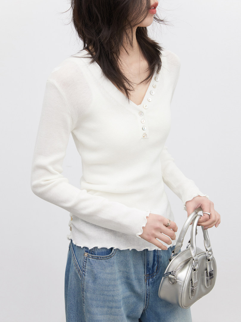 Woman wearing a white long-sleeve buttoned knit top with jeans and a silver handbag