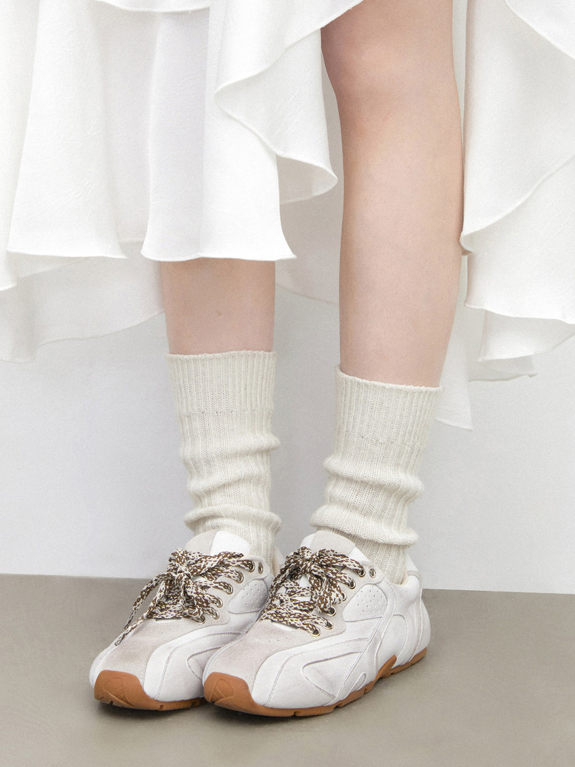 White sneakers worn with cream socks and a white skirt