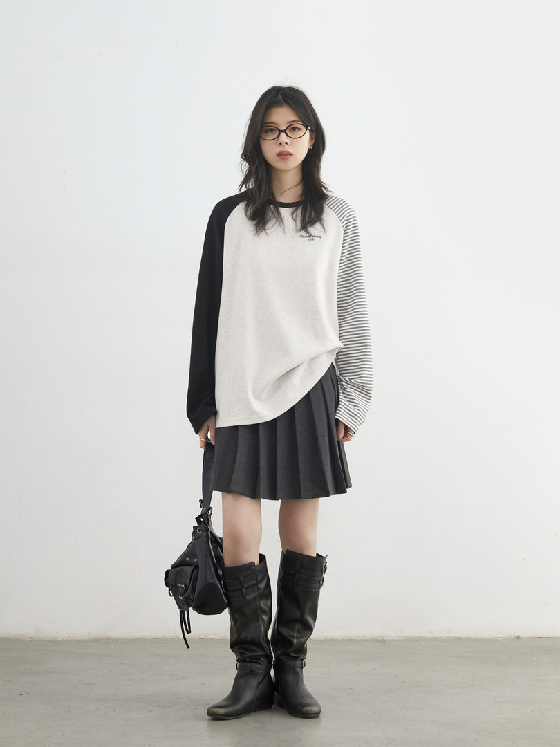 Model wearing a black-and-white long-sleeve top, pleated skirt, and black knee-high boots with a black bag