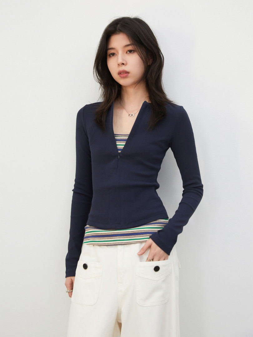 Model wearing a navy fitted long-sleeve top with striped layering and white pants