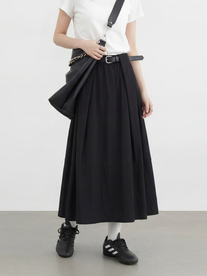 Model wearing a black pleated midi skirt styled with a white T-shirt and black sneakers
