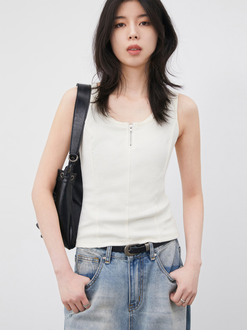Model wearing a white sleeveless zip-front top with light blue jeans and a black shoulder bag