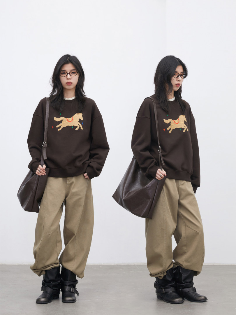 Model wearing a dark brown graphic sweatshirt with beige wide-leg pants and black boots