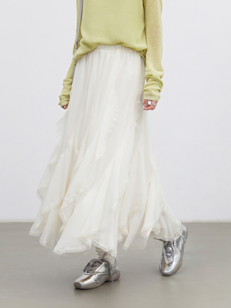 Model wearing a light green sweater, flowing white skirt, and silver shoes