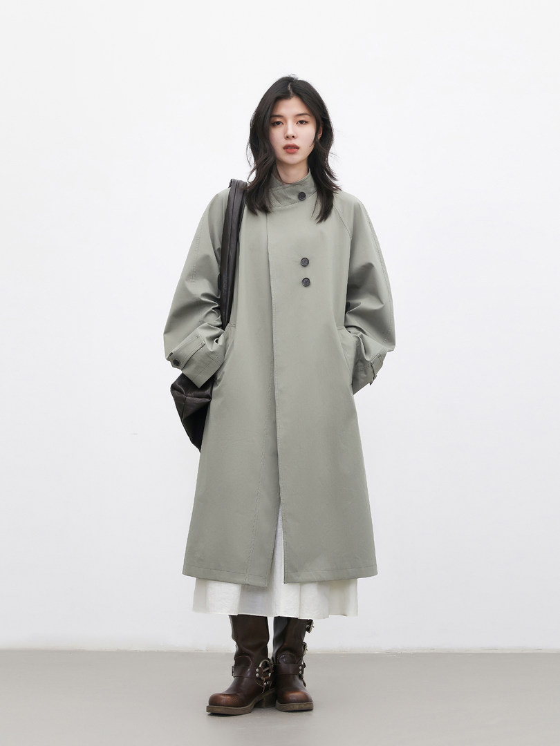 Model wearing a light gray long coat with dark boots on a plain background