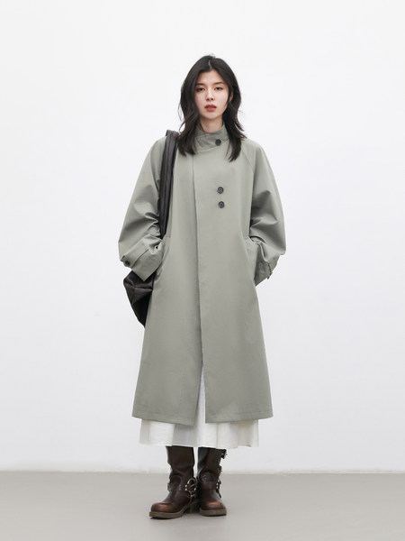 Model wearing a light gray long coat with dark boots on a plain background