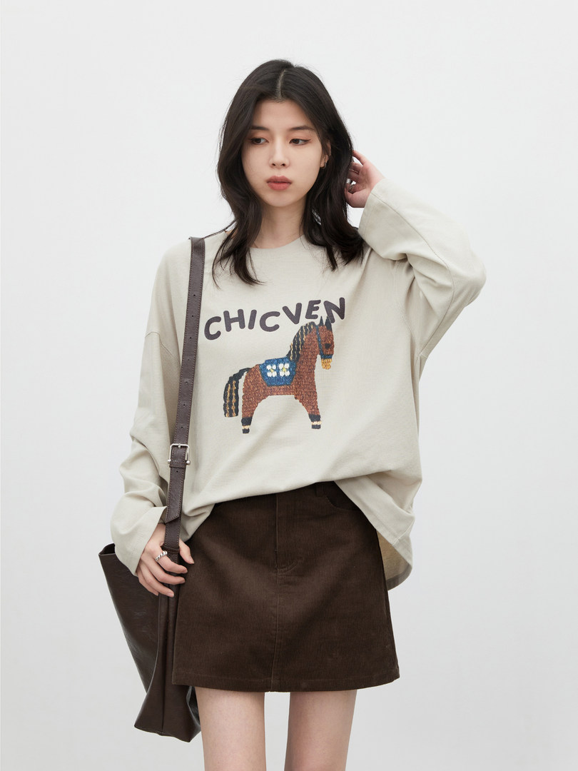 Model wearing a beige graphic sweater with a brown skirt and shoulder bag