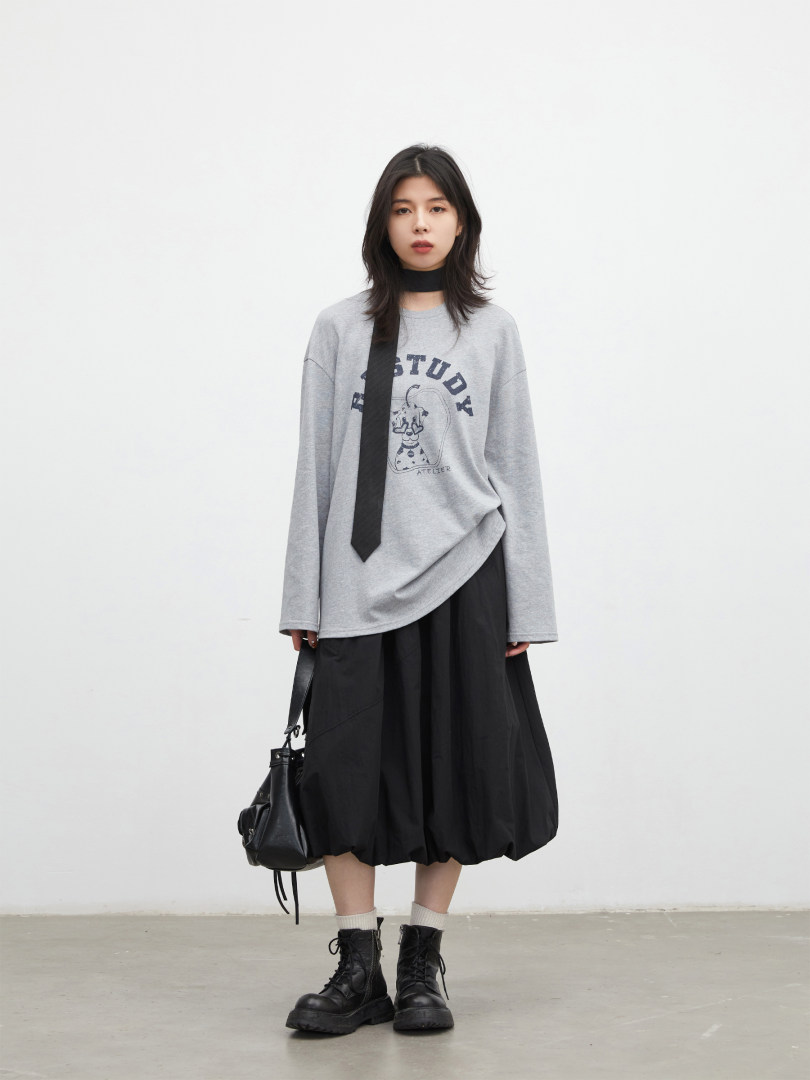 Model wearing a gray graphic sweatshirt with a black skirt, combat boots, and a shoulder bag.