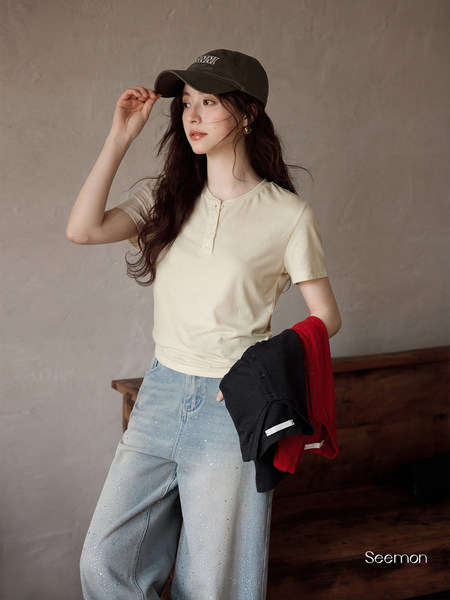 Woman modeling a beige short-sleeve top with light blue jeans and a black cap