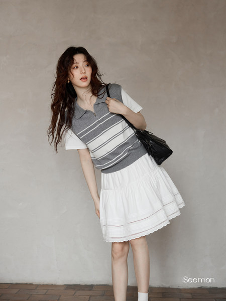 Model wearing a gray striped knit vest layered over a white T-shirt with a white skirt and black shoulder bag