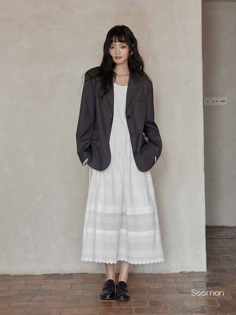 Model wearing a dark blazer over a white midi dress with black loafers