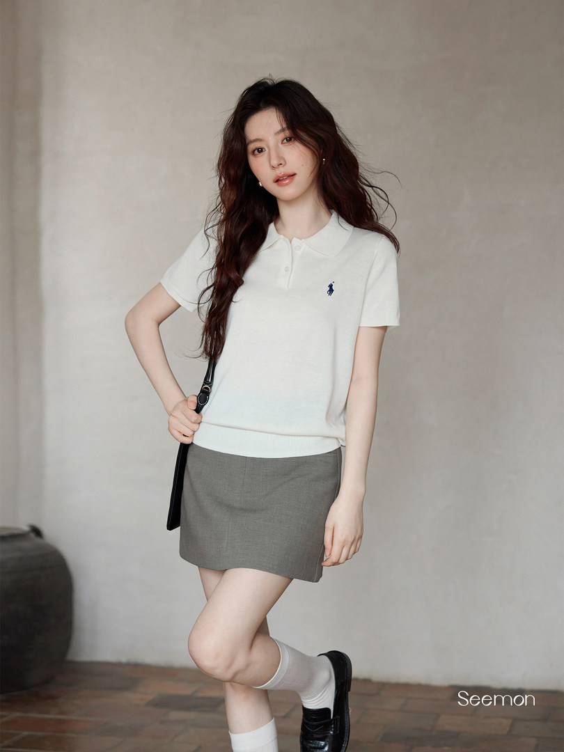 Woman modeling a white polo shirt with a gray mini skirt and black loafers