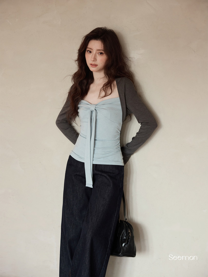Model wearing a light blue strapless tie-front top with dark sleeves and wide-leg jeans