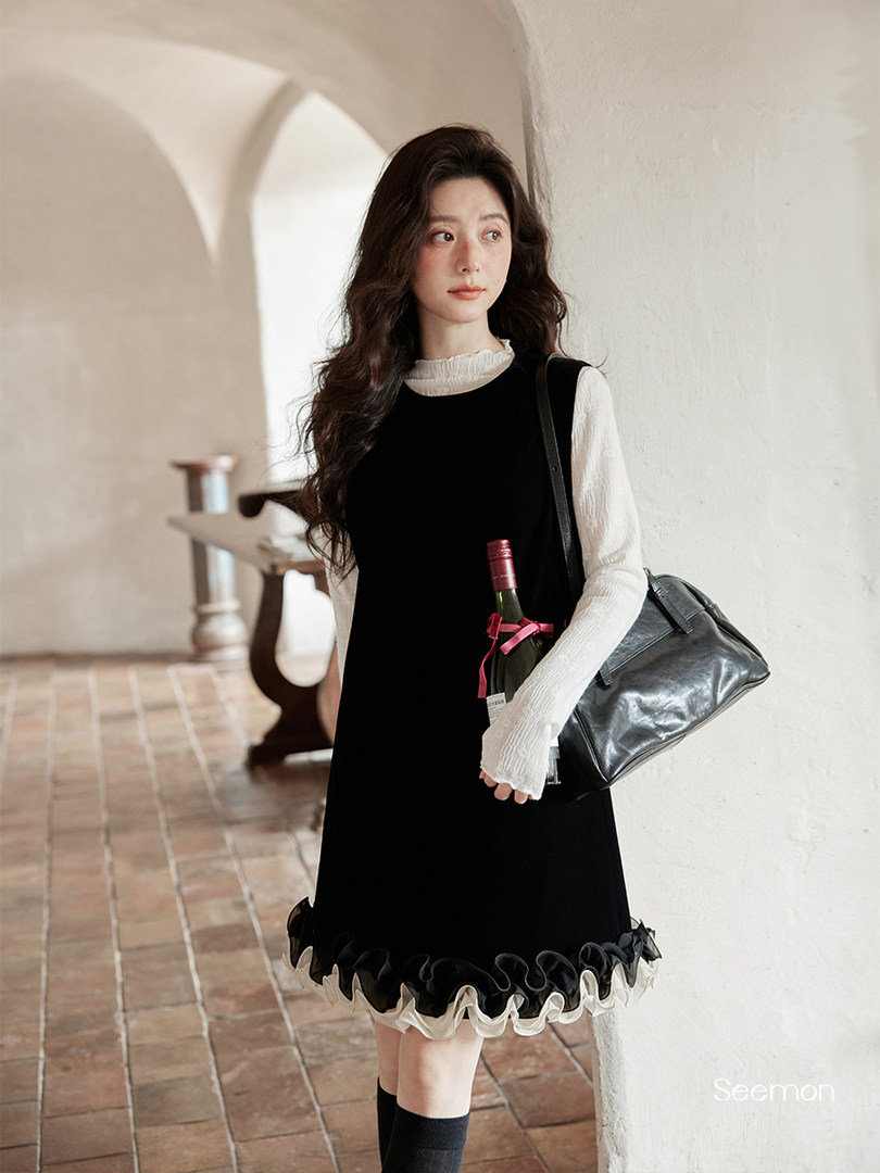 Model wearing a black dress with white ruffled blouse and carrying a black handbag