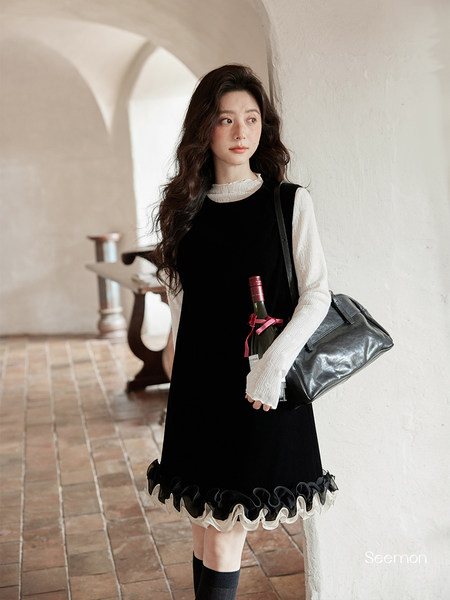 Model wearing a black dress with white ruffled blouse and carrying a black handbag