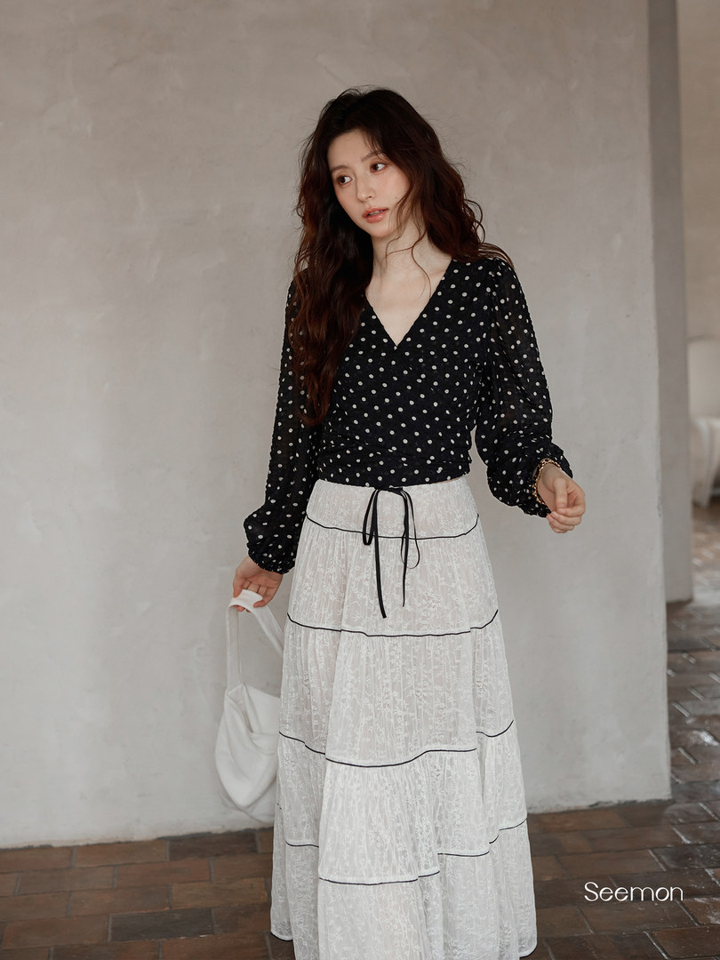 Model wearing a black polka dot blouse with a white tiered lace skirt
