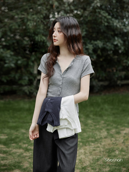 Woman wearing a gray short-sleeve button-front top with dark pants outdoors