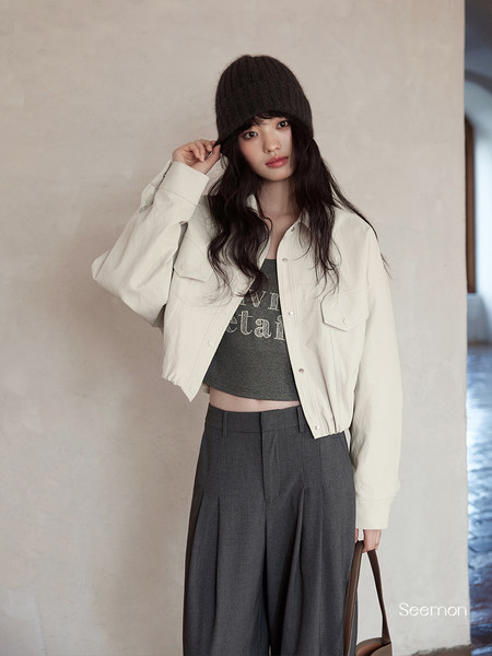 Model wearing a cream cropped jacket with dark wide-leg pants and a black knit hat
