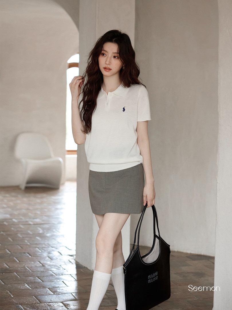 Woman wearing a white polo top and gray mini skirt while holding a black tote bag