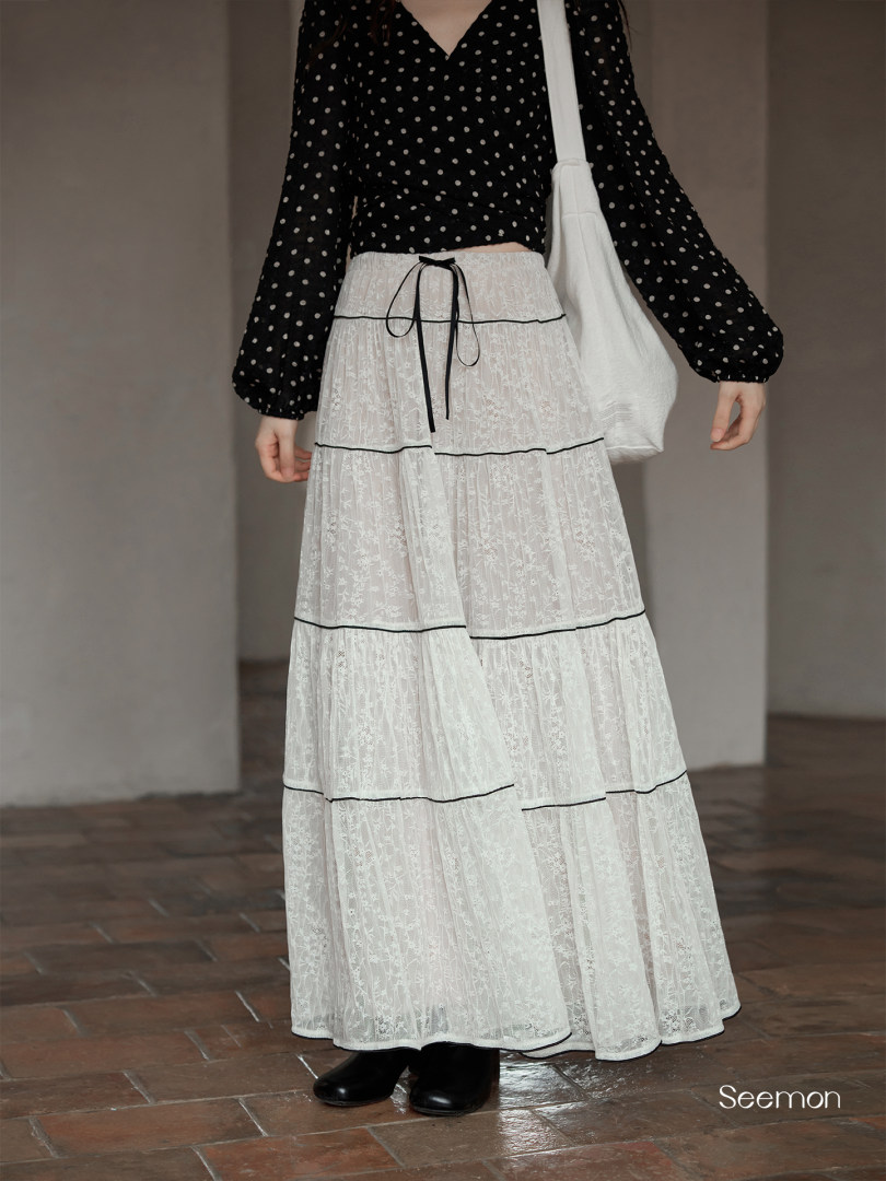 Model wearing a black polka dot top with a white tiered lace maxi skirt and shoulder bag