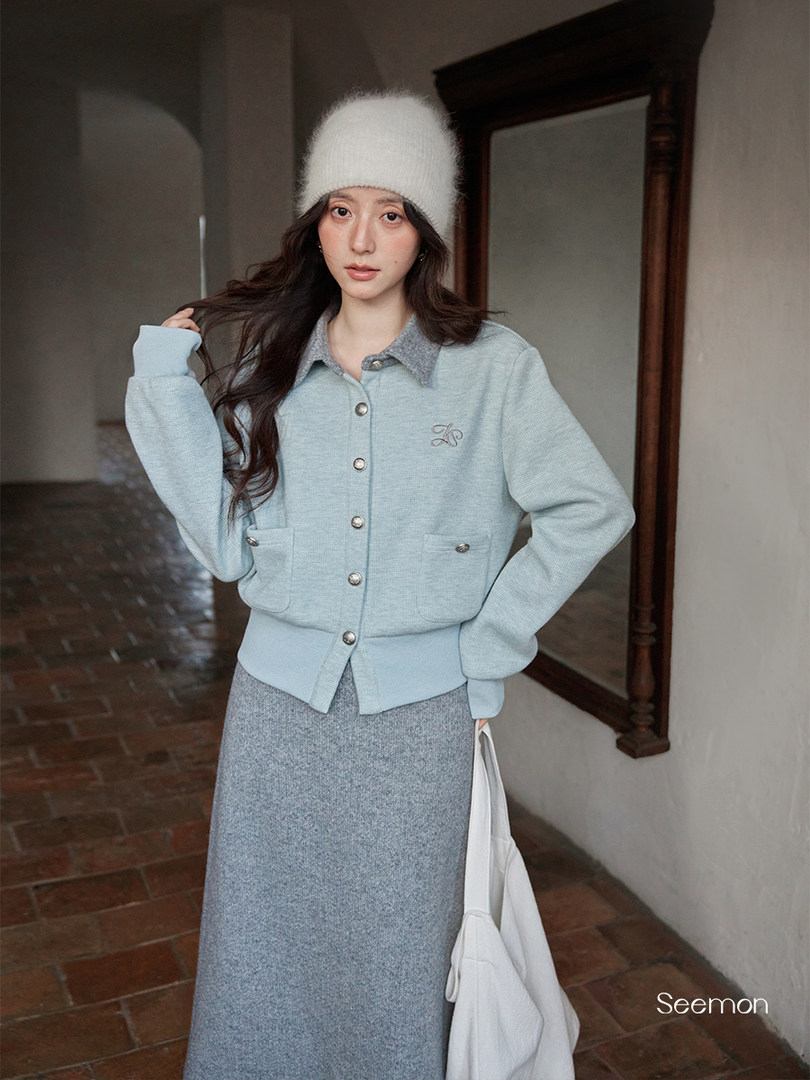 Model wearing a light blue knit button-up jacket and matching gray skirt with a white fuzzy hat