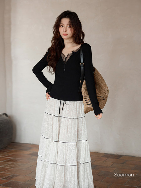 Model wearing a black lace-trim long-sleeve top with a white lace maxi skirt and straw bag