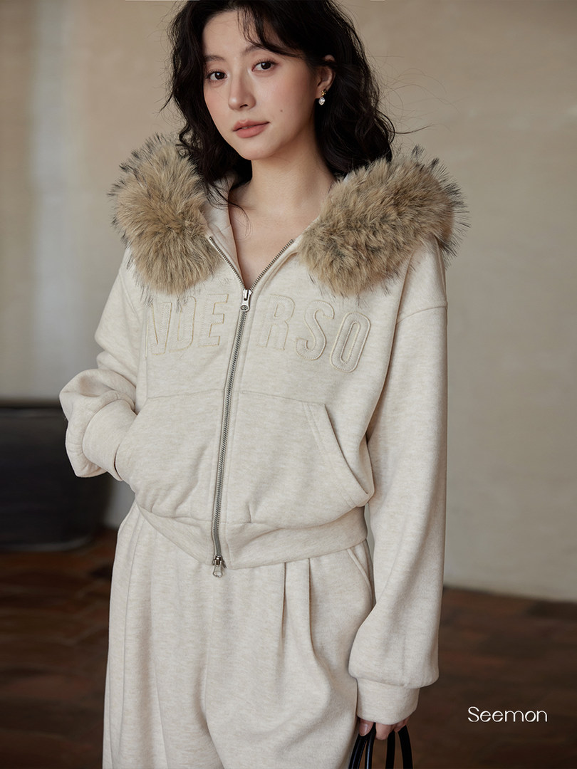 Woman wearing a cream zip-up hoodie and matching sweatpants with a fur-trimmed hood