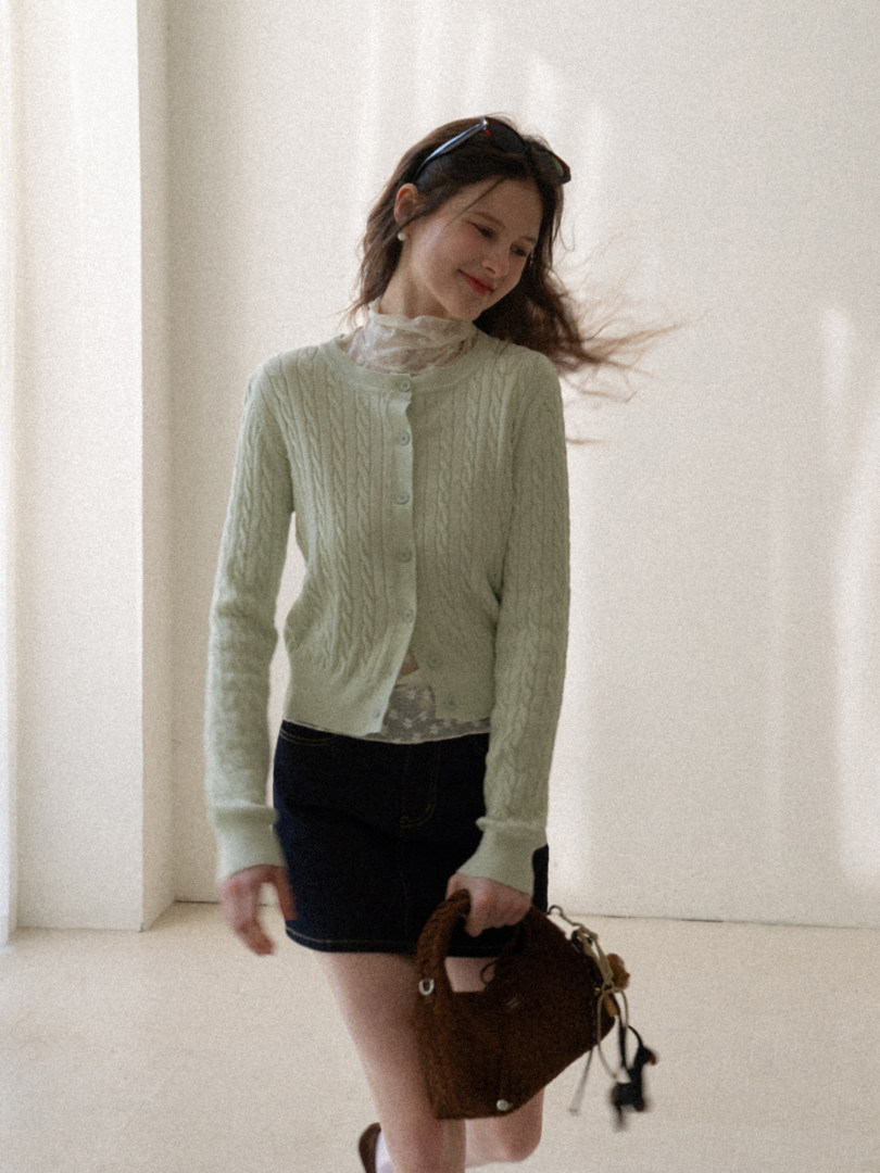 Model wearing a light green cable-knit cardigan with a brown handbag