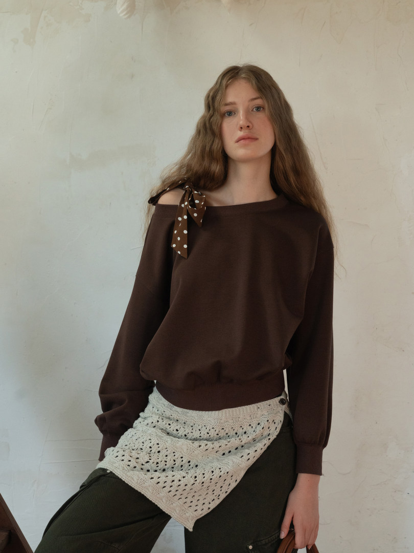 Model wearing a brown off-shoulder long-sleeve top with a polka dot bow detail