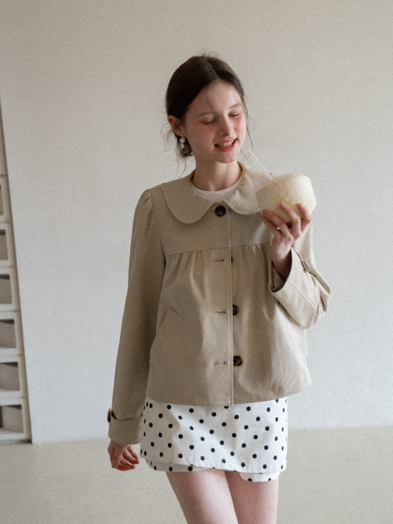 Model wearing a beige collared jacket with a white polka dot skirt