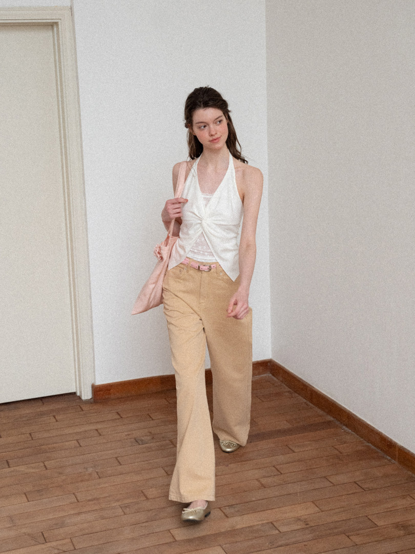 Model wearing a white halter top with beige pants and a pink bag