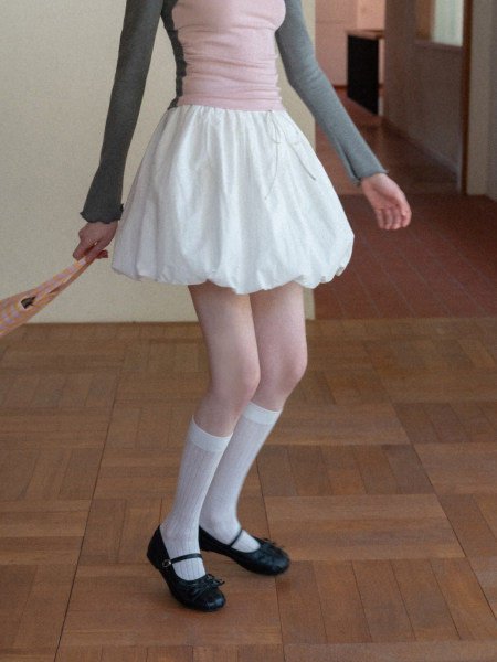Model wearing a pink-and-gray long-sleeve top with a white bubble skirt and black Mary Jane flats